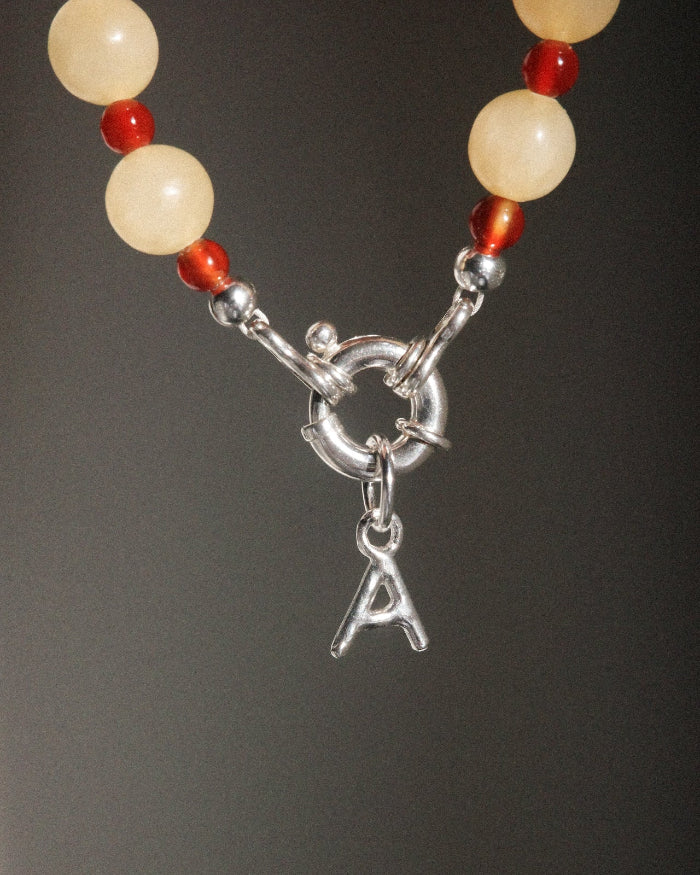 Necklace with beads and a silver clasp with a 'A' charm on a dark background