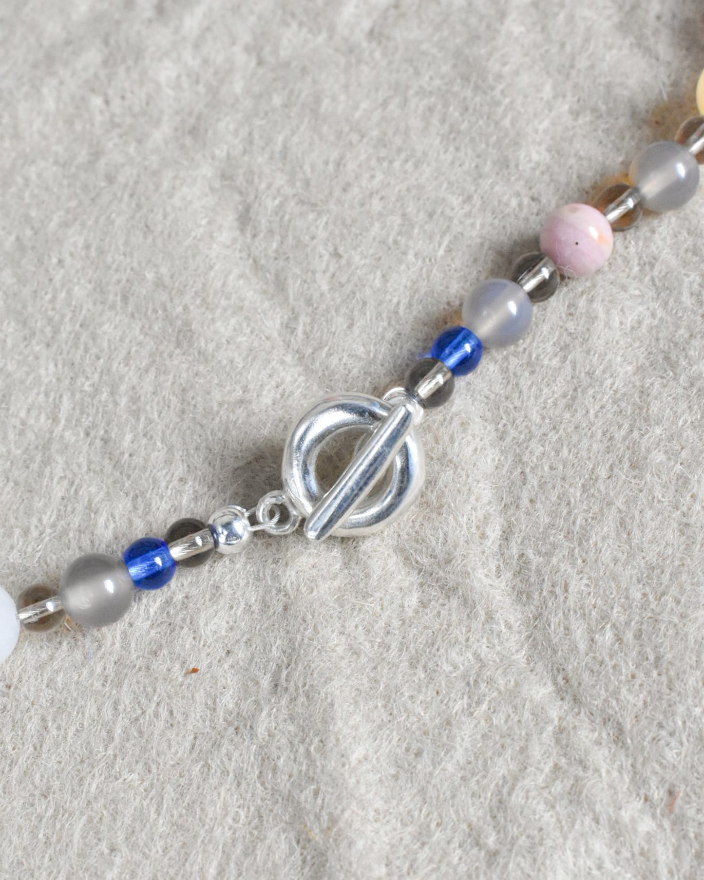a colourful beaded necklace in a neutral brown grey base with coloirful stone and glass beads scattered. blue jade, agate, carnelian, aventurine. finished with solid recycled silver doughnut toggle clasp.