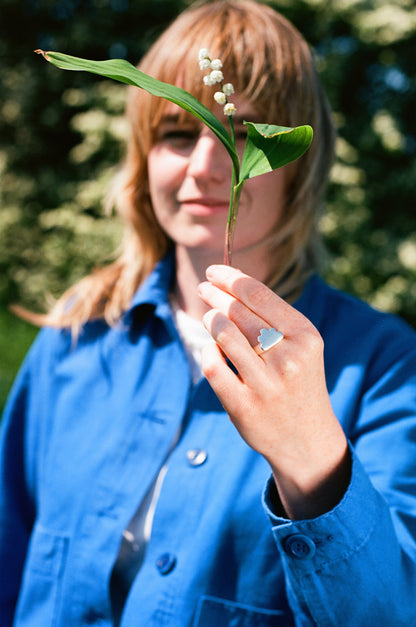 a woman in a royal blue paynter jacket holds a lily of the valley flower and wears a shining solid recycled silver signet ring in the shape of a cloud