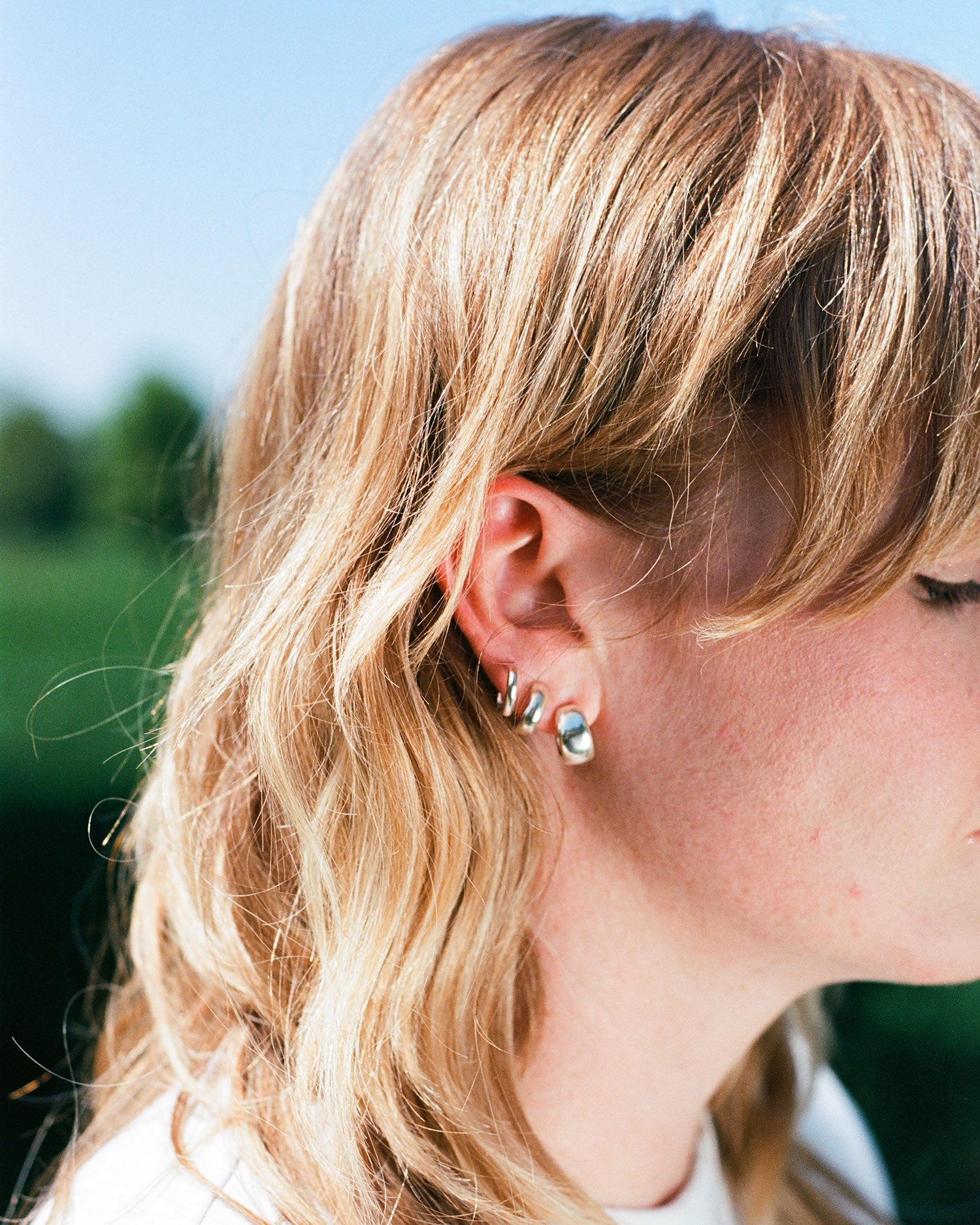 a woman wears three earrings in her ears. smooth round minimal huggy hoop earrings. solid eco recycled silver with push backs.