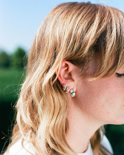 a woman wears three earrings in her ears. smooth round minimal huggy hoop earrings. solid eco recycled silver with push backs.