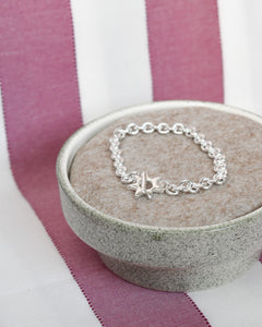 a cushioned dish holds a solid recycled silver heavy quality chain bracelet with hand carved star shaped toggle clasp