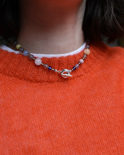 a colourful beaded necklace in a neutral brown grey base with coloirful stone and glass beads scattered. blue jade, agate, carnelian, aventurine. finished with solid recycled silver doughnut toggle clasp.