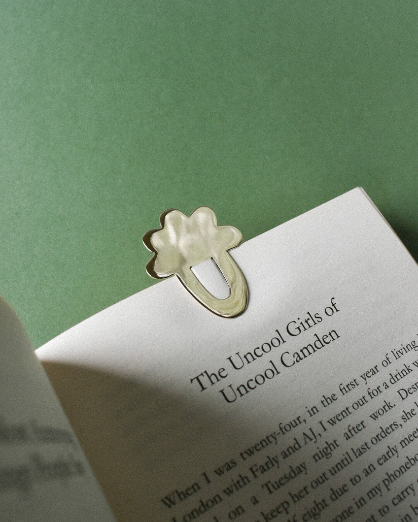 a book with a brass bookmark in the shape of a cloud. paper clip style with scalloped flower edge that keeps page in book. gold toned metal with shiny polish finish.