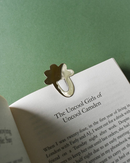 a book with a brass bookmark in the shape of a cloud. paper clip style with scalloped flower edge that keeps page in book. gold toned metal with shiny polish finish.